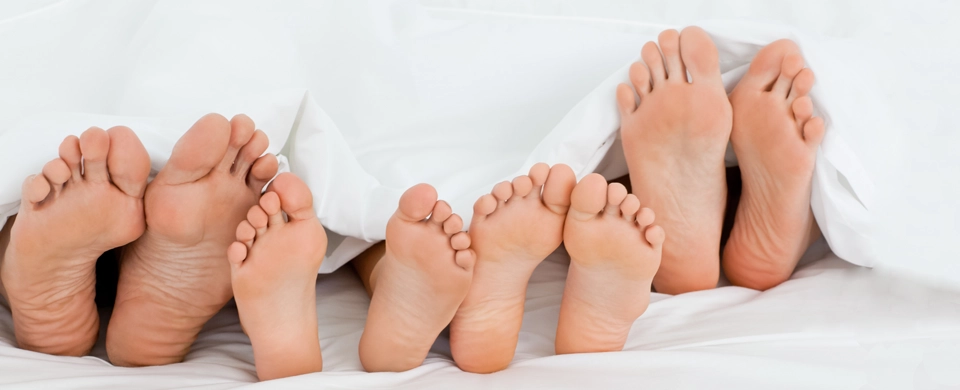 Multiple bare feet under white sheets, showing soles and toes. Multiple bare feet under white sheets, showing soles and toes.